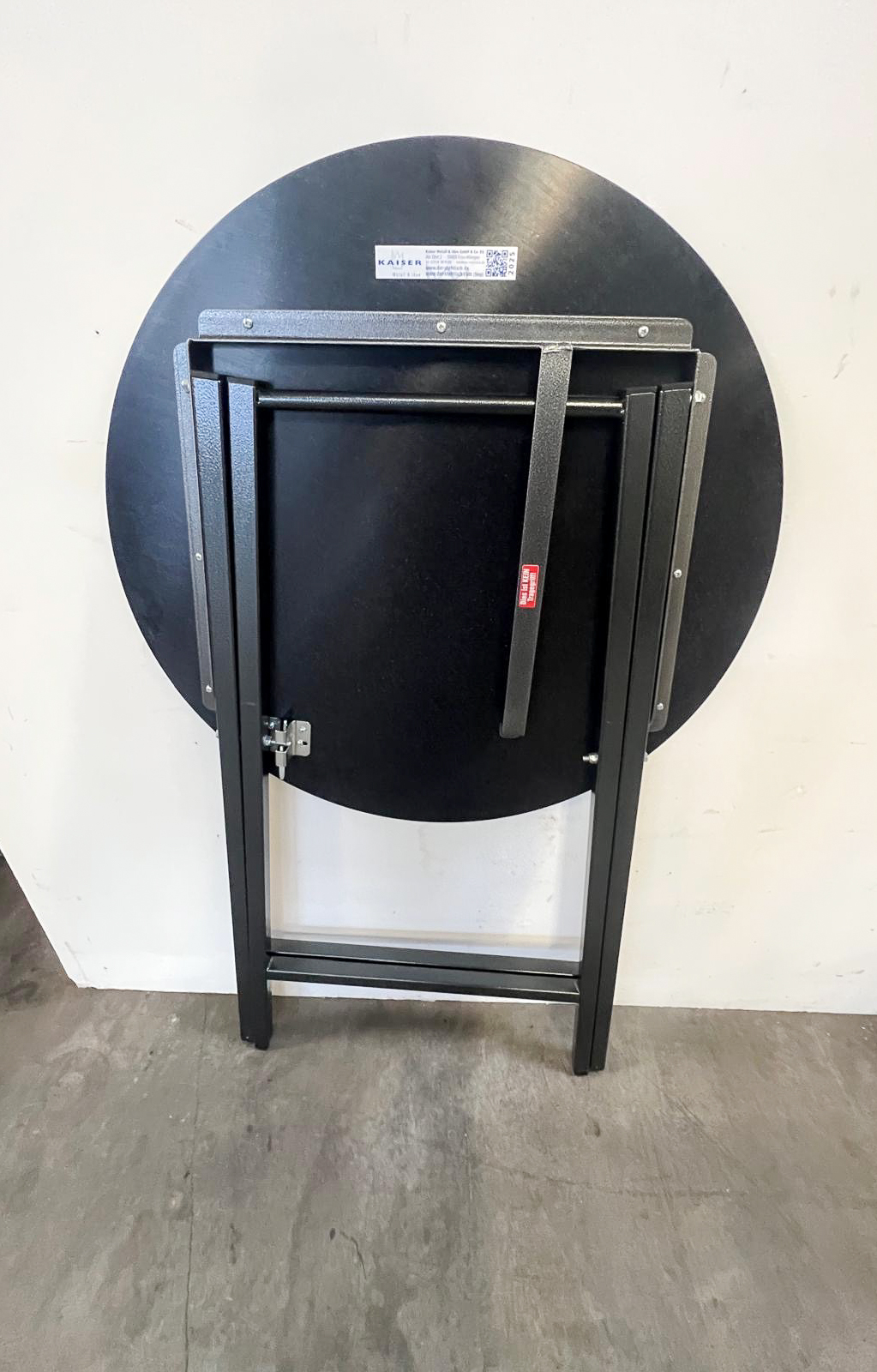 Unterseite des zusammengeklappten Scherenstehtisch ST-U80 Hammerschlag mit schwarzer Tischplatte und stabilem, hammerschlag-pulverbeschichtetem Stahlgestell.